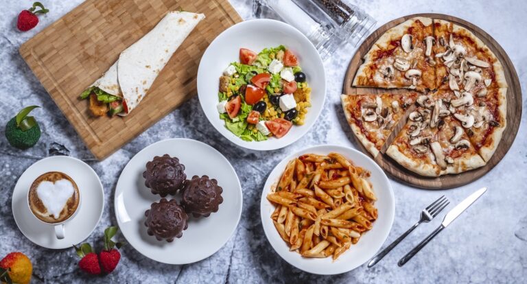 A delicious spread of food including pizza, pasta, salad, a wrap, and desserts on a table.